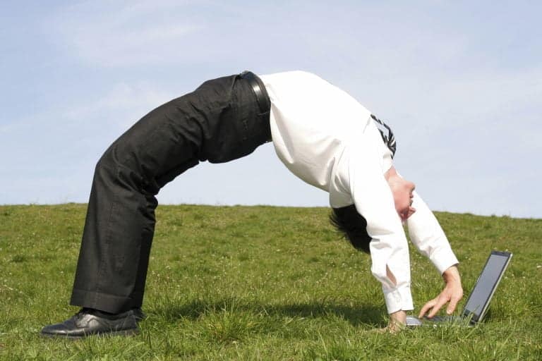 The image shows a businessman bending over backward while using a laptop.